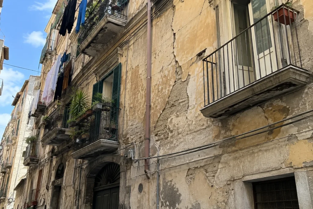 Facciata di un vecchio palazzo residenziale napoletano con crepe e intonaco deteriorato, immagine illustrativa dello sgombero di undici famiglie.